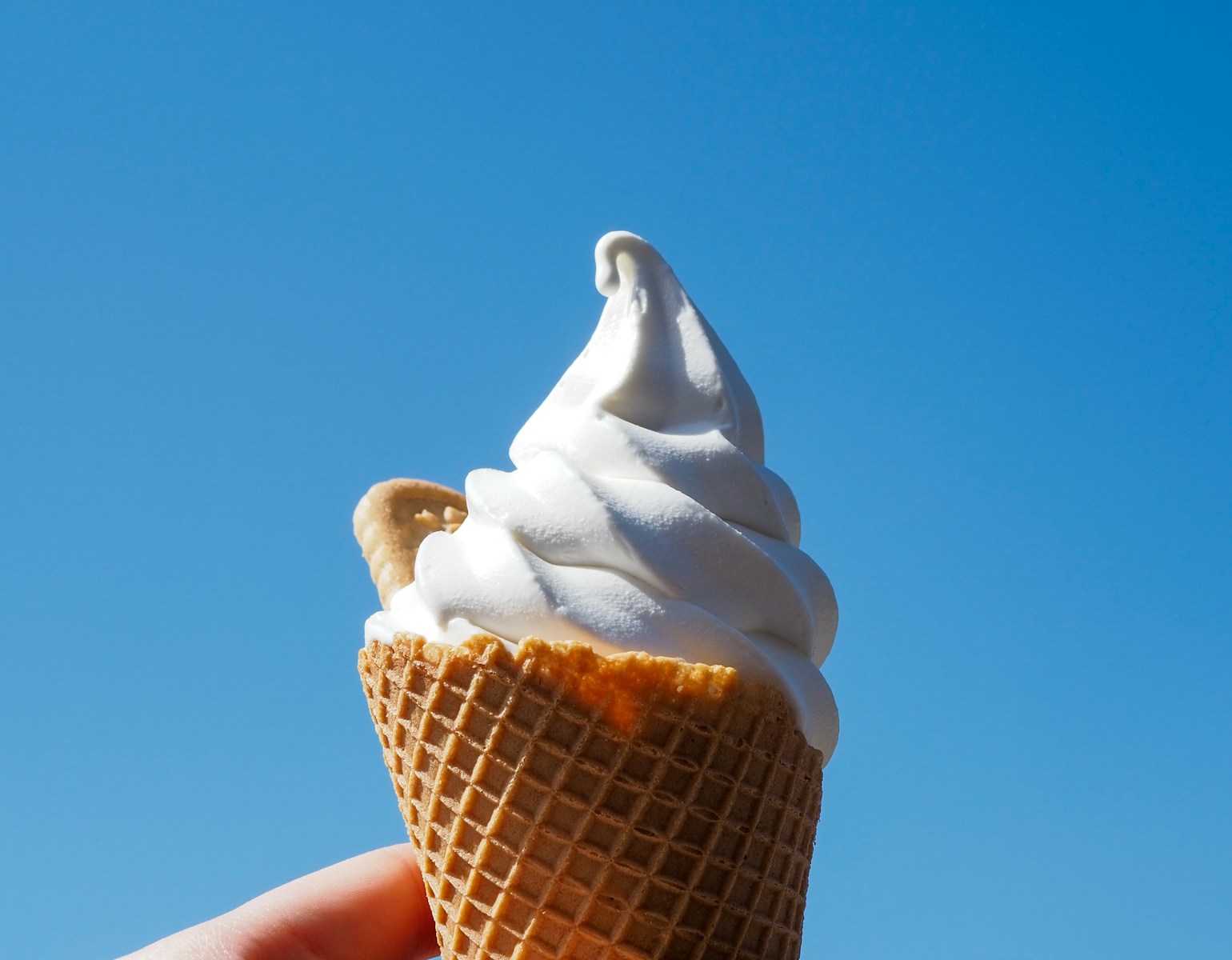 a hand holding an ice cream cone in front of a blue sky